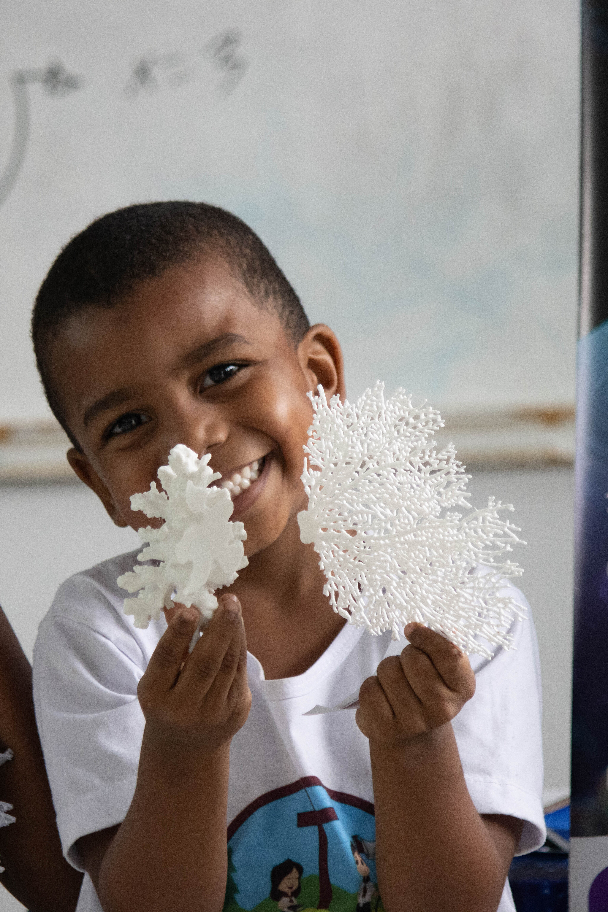 Criança sorri segurando dois modelos brancos de corais impressos em 3D