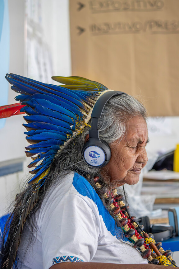 Mulher indígena usa fones de ouvido do Projeto Mar de Sentidos durante uma exposição