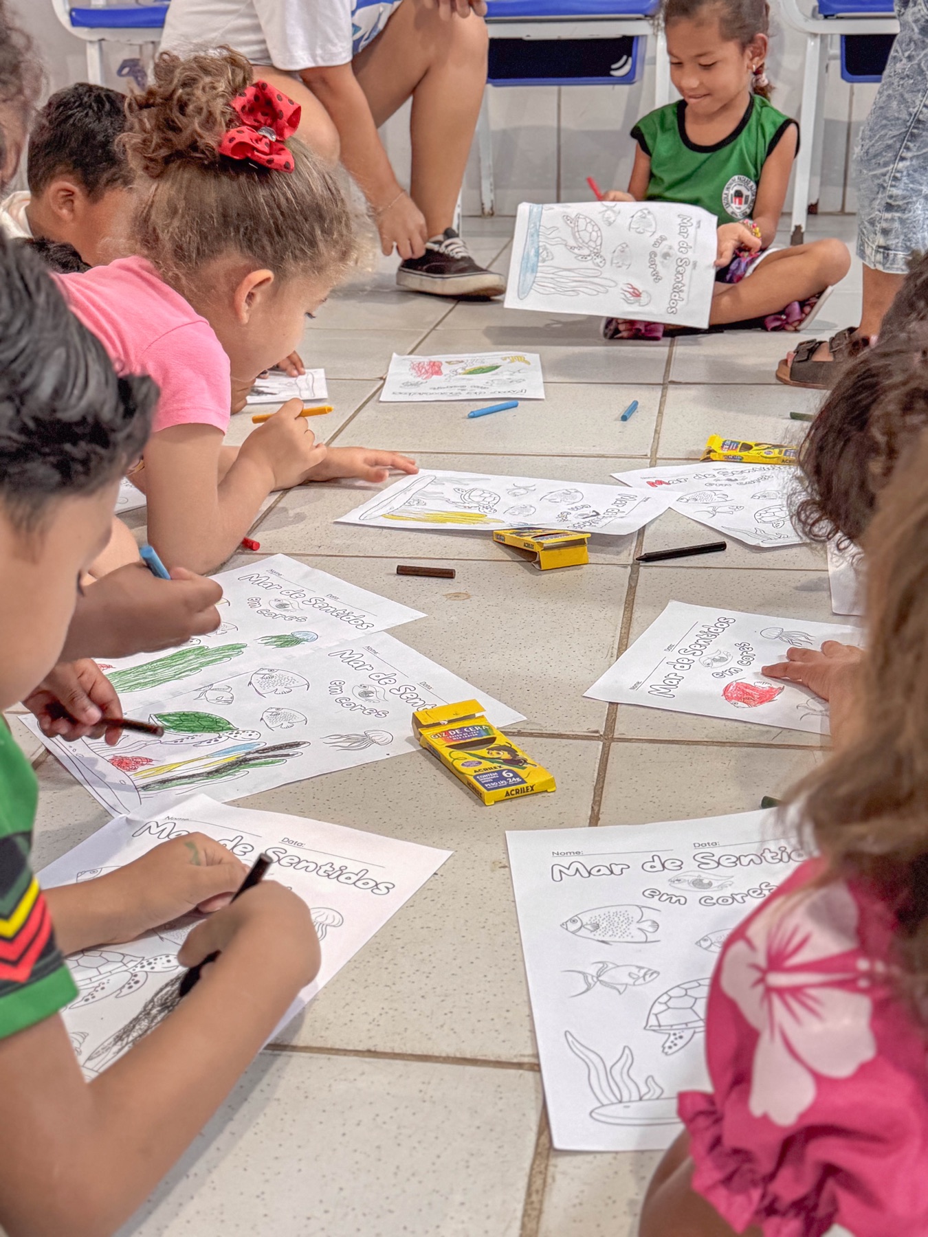 Grupo de crianças colore atividades sobre animais e paisagens marinhas no chão da sala
