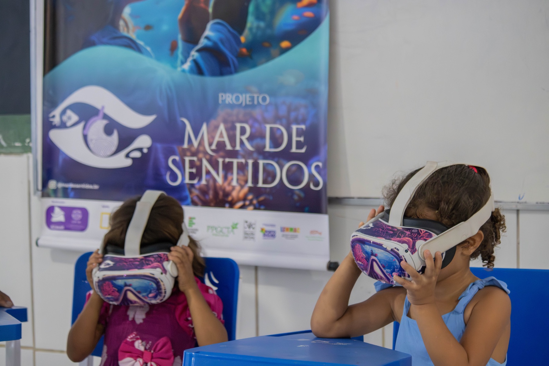 Duas crianças utilizam óculos de realidade virtual diante do painel Mar de Sentidos