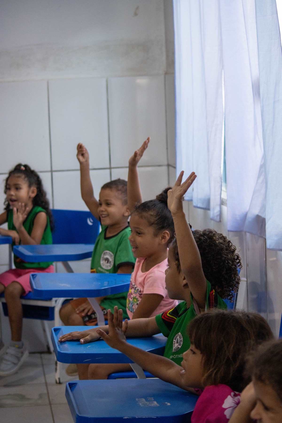 Crianças participam ativamente de uma conversa em sala de aula com as mãos levantadas