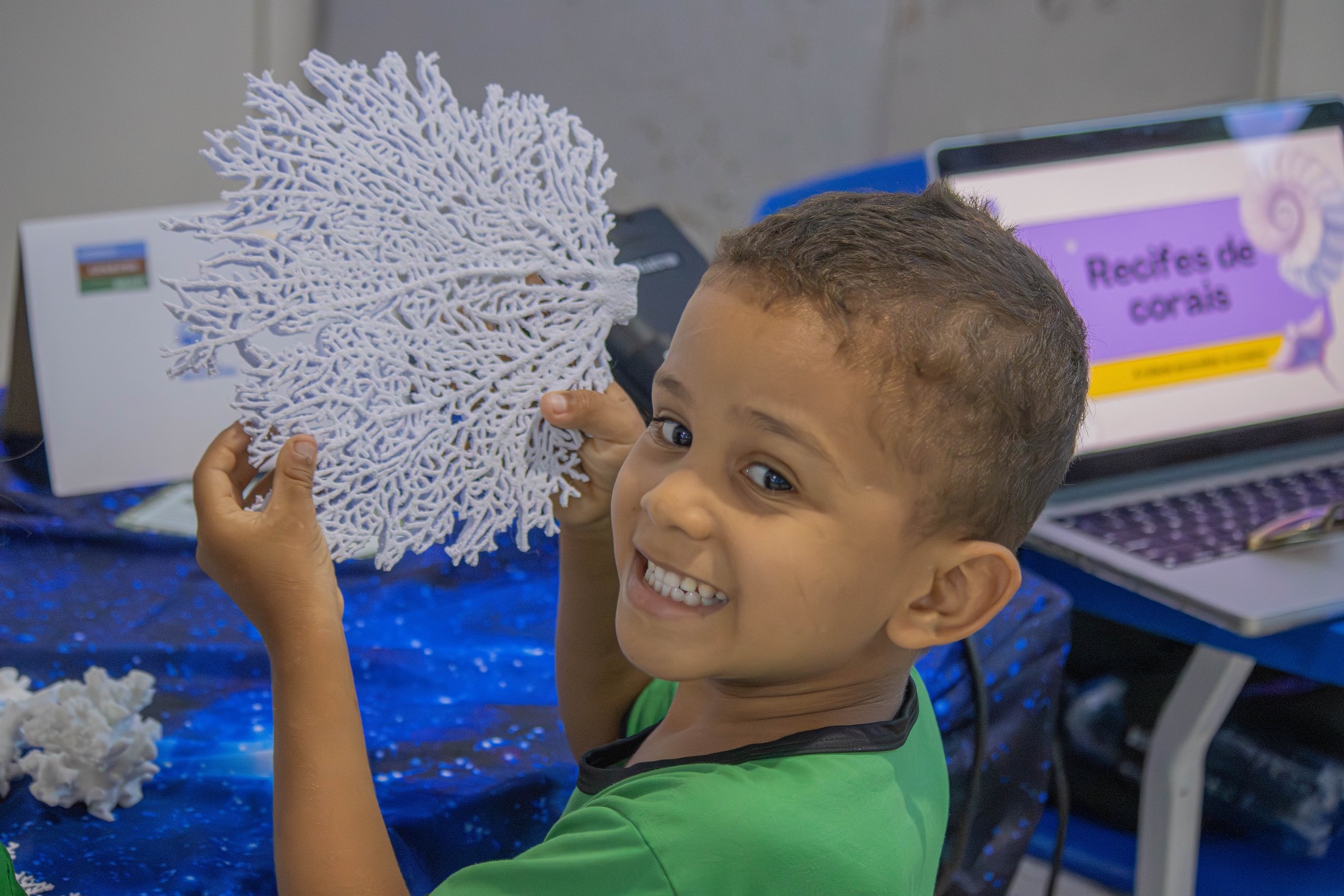 Criança sorri ao segurar um grande modelo tridimensional branco de coral