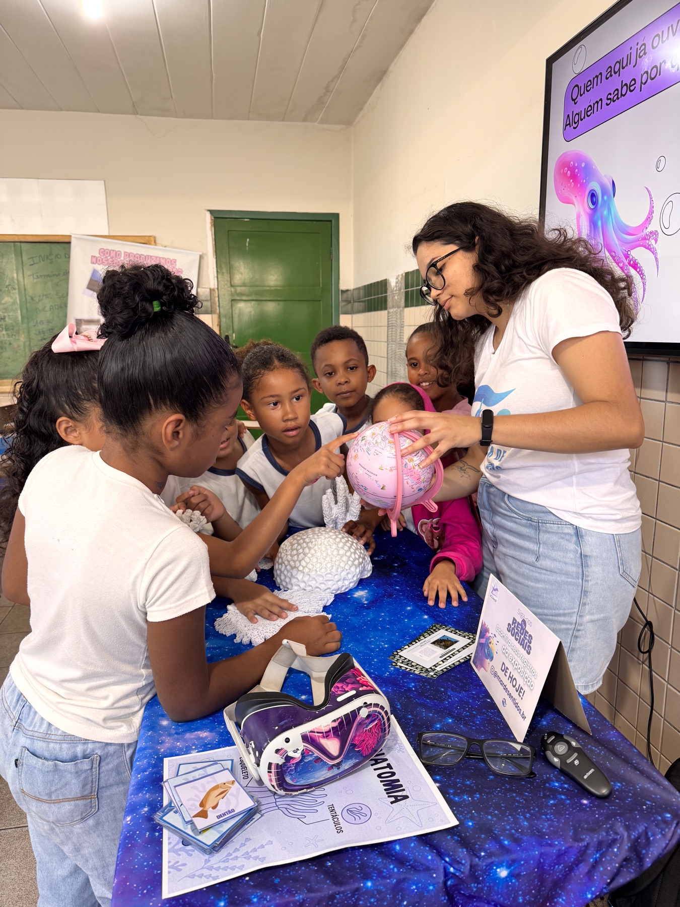 Educadora apresenta um globo terrestre a crianças reunidas ao redor de modelos de corais