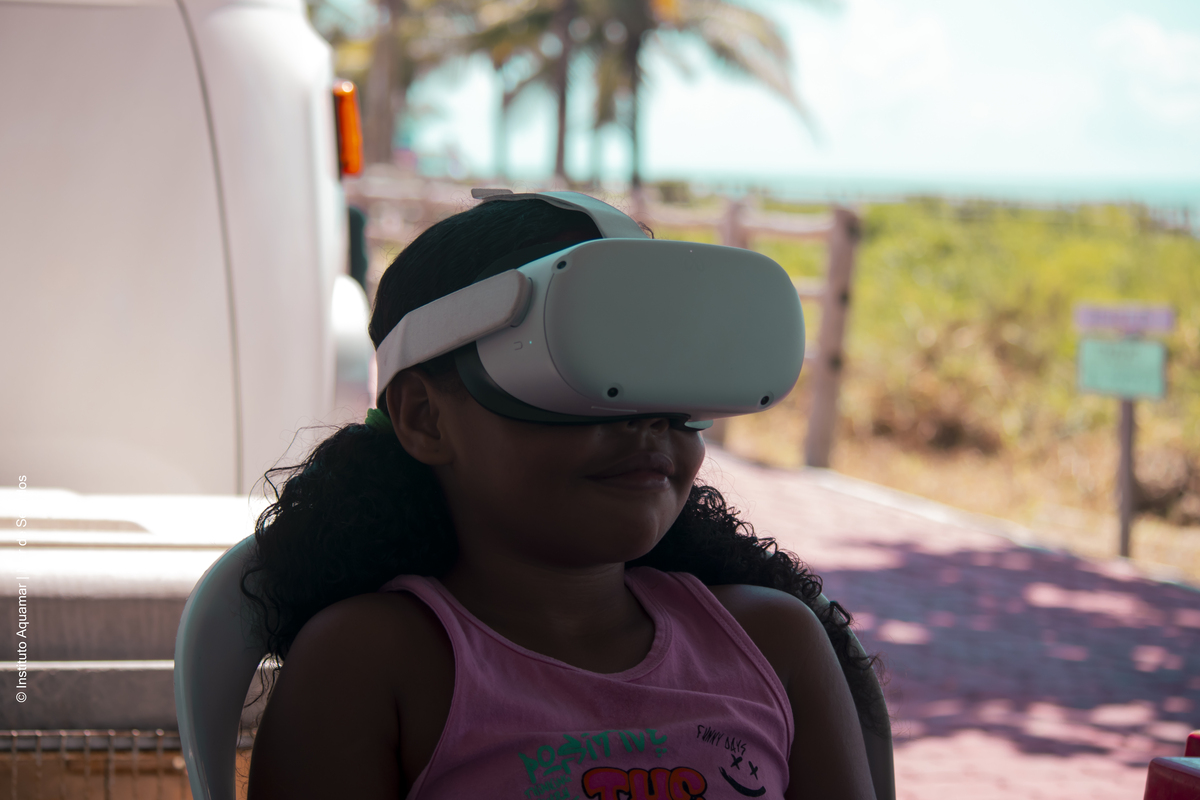 Criança utiliza óculos de realidade virtual em uma exposição próxima à praia